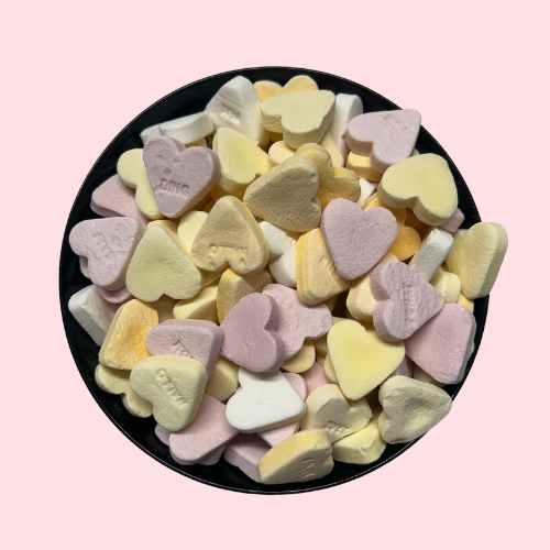 Roze, gele en witte vruchtenhartjes snoepjes met lieve berichtjes in zwart bakje