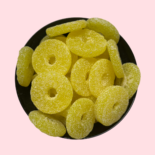 Gesuikerde zure gele ananasschijven met gat in het midden in zwart bakje